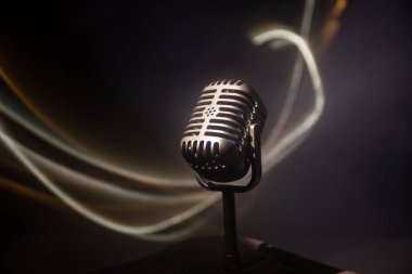 Ses, müzik için mikrofon, ses stüdyosunda ya da sahnede karaoke. Mikrofon teknolojisi. Konuşma yayın ekipmanı. Karanlık odadaki mikrofon, arka farlı masanın üstünde. Seçici odak