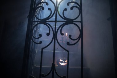 Korku Cadılar Bayramı konsepti. Ürkütücü terk edilmiş kale. Eski bir şamdan ve cadılar bayramı balkabağı tahta merdivenlerde parlıyor ve geceleri kafes kapılı. Arkaplan ışığı ve sisli dekorasyon. Seçici odak