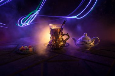 Arap çayı bardakta, doğu aperatifleriyle birlikte koyu arkaplanda, ışık ve dumanlı taş bir zemin üzerinde. Doğu çay konsepti. Seçici odak.
