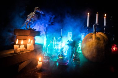 Büyücü masası. Korku Cadılar Bayramı konsepti. Şişelerdeki sihirli iksirler ahşap masada kitaplar ve mumlarla. Karanlık tonlu sisli arka planda farklı elementlerle cadılar bayramı natürmortu. Seçici odak
