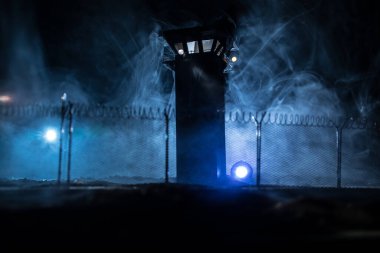 Criminal justice imprisonment concept. Old prison watchtower protected by wire of prison fence at night. Creative art decoration. Selective focus clipart