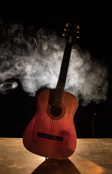 Концепция музыки. Акустическая гитара изолирована на тёмном фоне под лучом света с дымом с копировальным пространством. Гитарные струны, закройте. Селективный фокус
.