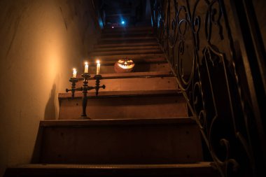 Korku Cadılar Bayramı konsepti. Ürkütücü terk edilmiş kale. Eski bir şamdan ve cadılar bayramı balkabağı tahta merdivenlerde parlıyor ve geceleri kafes kapılı. Arkaplan ışığı ve sisli dekorasyon. Seçici odak