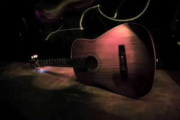 Music concept. Acoustic guitar isolated on a dark background under beam of light with smoke with copy space. Guitar Strings, close up. Selective focus.