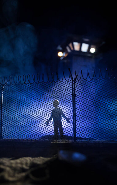 Criminal justice imprisonment concept or prison break concept. Silhoette of prisoner standing near of prison fence with watchtower at night. Creative art decoration. Selective focus