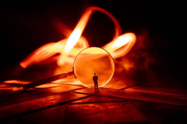 Karanlık arka planda, taş yüzeyde büyüteç, aydınlık altında, gizemli dedektif konsepti. Dev büyüteçin yanında duran bir kişinin silueti.