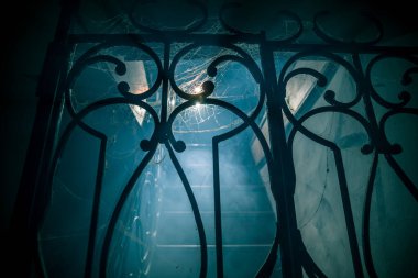 Korku Cadılar Bayramı konsepti. Ürkütücü terk edilmiş kale. Eski bir şamdan ve cadılar bayramı balkabağı tahta merdivenlerde parlıyor ve geceleri kafes kapılı. Arkaplan ışığı ve sisli dekorasyon. Seçici odak