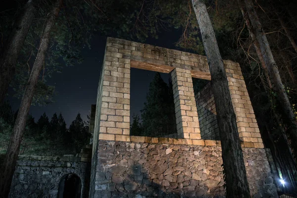 Old abandoned building in forest, Facade ruins of industrial factory. Spring long pine forest at night