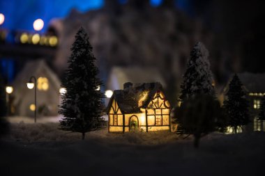 Kışın karlı küçük dekoratif evler, Noel ve yeni yıl minyatür evleri geceleri karlı köknar ağaçları. Tatil konsepti. Seçici odak