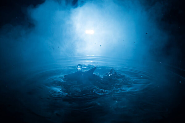 Абстрактное понятие. Силуэт рыб (акул), прыгающих по воде ночью. Вода брызгает на темном туманном фоне. Селективный фокус.