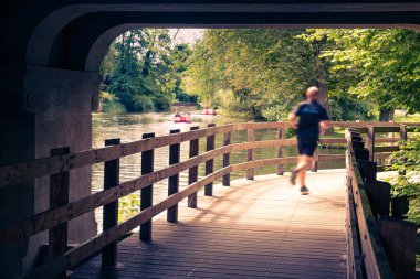 Odense Nehri boyunca koşan bir adam. Kıyılar, başta kayın ağaçları olmak üzere çeşitli ağaçlarla kaplıdır..