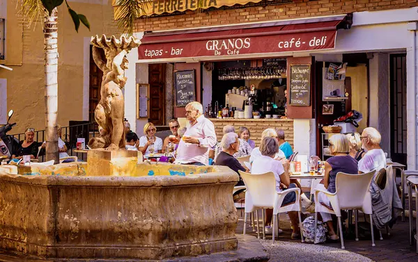 Almunecar 'ın merkezindeki Plaza Higuitos' ta ortasında çeşme olan küçük bir kafe. Turistler ve yerliler güneşin altında kahvelerini ve atıştırmalıklarını yiyorlar..