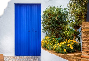 Frigiliana 'da turuncu çiçeklerin yanındaki çok mavi bir kapı. Frigiliana, Malaga 'nın doğusundaki Akdeniz kıyısında yer almaktadır.