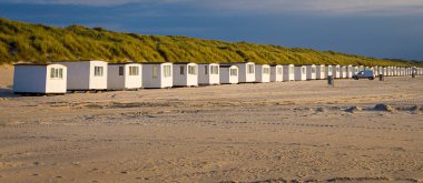 Panoramic view of long row of privately owned beach houses at the Danish Weast-coast by Lokken. The warm afternoon sun is casting a warm glow over the houses and the sand dunes behind. clipart