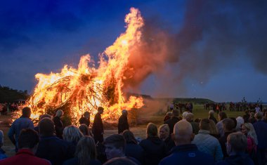 Büyük bir grup insan yaz ortasını bir İskandinav ülkesinde büyük bir şenlik ateşi yakarak kutluyor. .