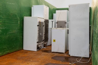 Eski, yıpranmış uzun buzdolapları geri dönüşüm istasyonundaki büyük yeşil bir konteynırın içine yerleştirilmiş. Atık yönetimi ve çevresel bakımı destekleyen cihazlar sorumlu bir şekilde atılıyor..