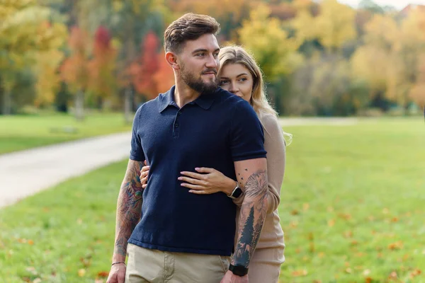 一位年轻貌美的孕妇在秋天的公园里依偎在一起 拥抱了她有男子气概的丈夫 — 图库照片