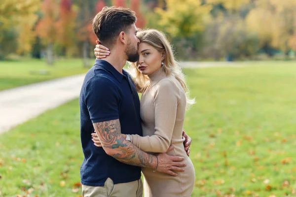一个英俊的男人在秋天的公园里温柔地亲吻着他美丽的年轻孕妇 拥抱着她 — 图库照片
