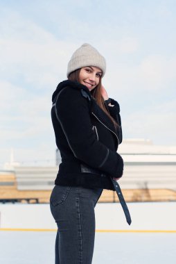 Şık cekette mutlu güzel bir kadın eğleniyor, buz pateni pistinde gülüyor. Neşeli genç bayan Noel buz pateni pistinde kayıyor. Kış tatili dışarıda