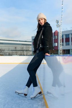 Şık cekette mutlu güzel bir kadın eğleniyor, buz pateni pistinde gülüyor. Neşeli genç bayan Noel buz pateni pistinde kayıyor. Kış tatili dışarıda
