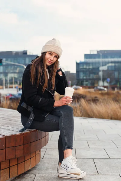 スマートフォンやコーヒーを持つかなりの女性の笑顔は ベンチに屋外に座って カメラを探してください 現代のライフスタイルのコンセプト ストックフォト