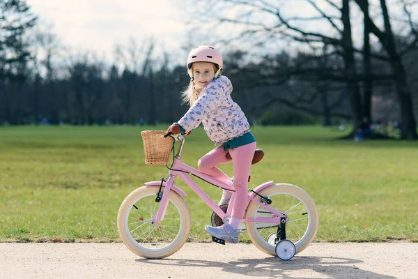 晴れた春の公園で安全なヘルメットで自転車に乗っている女の子 安全なヘルメットで自転車にバランスをとることを学ぶ未就学児 ストック写真