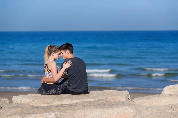 年轻夫妇相爱地坐在岩石沙滩上 望着地平线上的大海 爱情的概念 — 图库照片