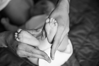 Yeni doğmuş bir bebeğin ayakları annelerin ellerinde. Mutlu aile kavramı. Anne, bebek bacaklarına sarıl. Siyah ve Beyaz.