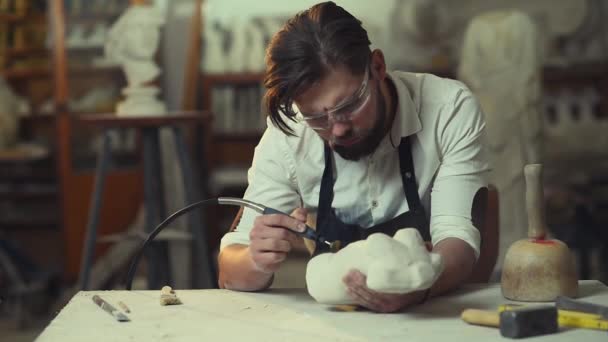 在他的创意作坊里 这位英俊而专注的现代胡子雕塑家正在研磨石雕 带着防护眼镜拿石头工作的年轻人 — 图库视频影像