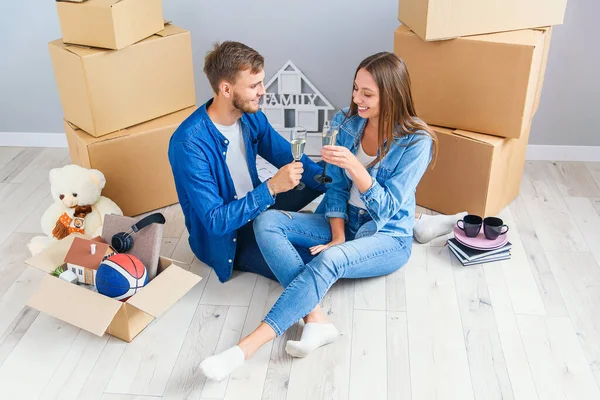 若いカップルは移動日に休憩を取って ダンボール箱に囲まれたシャンパンで祝う新しいアパートの床に座って ストック画像