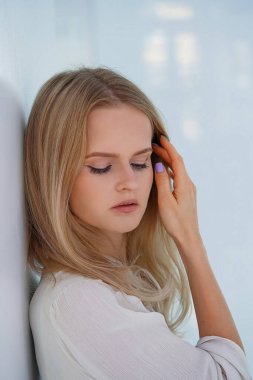 Saçına mor manikürlü baştan çıkarıcı genç bir kadının yakın plan portresi beyaz duvara yakın duruyor. Oldukça sağlıklı genç bir bayan. Beyaz iç kısımda açık renk yüz makyajı var.