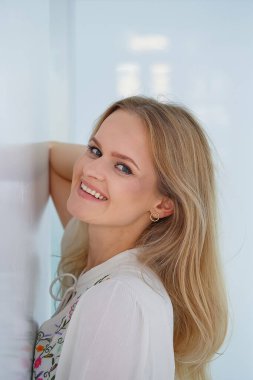 Çekici, gülümseyen, gülümseyen sarışın bir kadının yakından çekilmiş portresi. Oldukça sağlıklı genç bir bayan. Beyaz iç kısımda açık renk yüz makyajı var..
