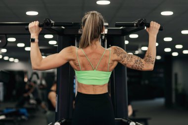 Spor salonunda spor yapan, sırt kasları için barfiks çeken bir kadın. Atletik kız eğitimi.