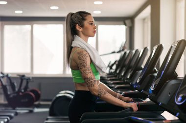 Spor salonunda koşu bandında egzersiz yapan güzel kaslı kadının yan görüntüsü..