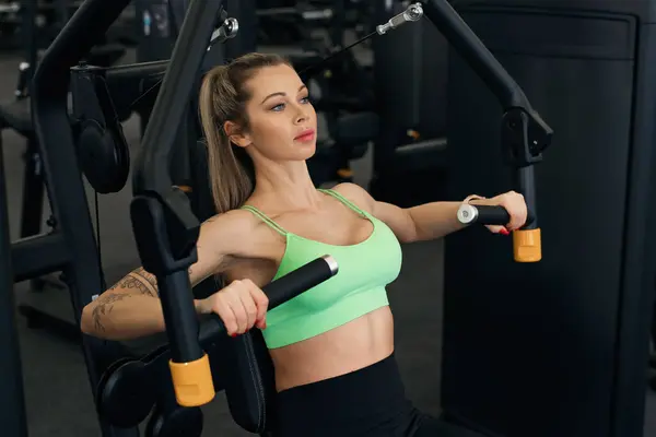 Young and sporty woman exercising chest press machine in modern gym.