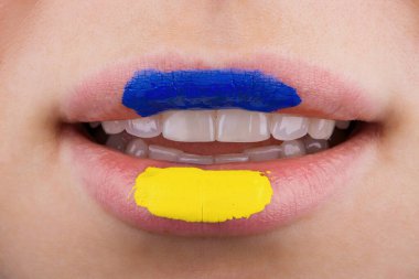 Mavi ve sarıya boyanmış güzel ve tombul kadın dudaklarına yakın çekim. Ukrayna bayrağı renginde tanımlanamayan bir kadının dudakları.