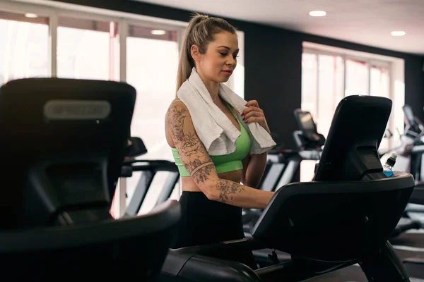 Side view of beautiful muscular woman with towel on neck exercising on treadmill at the gym.