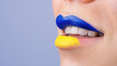 Mavi ve sarıya boyanmış güzel ve tombul kadın dudaklarına yakın çekim. Ukrayna bayrağı renginde tanınmayan bir kadının dudakları. İzole edilmiş arkaplan