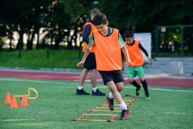 Profesyonel futbol antrenörü öğrencilerini izliyor. Futbol sahasındaki engellerin üstesinden gelerek koşma egzersizleri yapıyor.