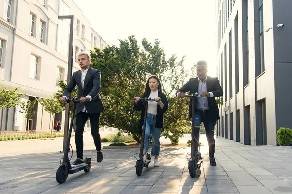 Confident multiracial office colleagues discussing business project go near office building with electric scooters