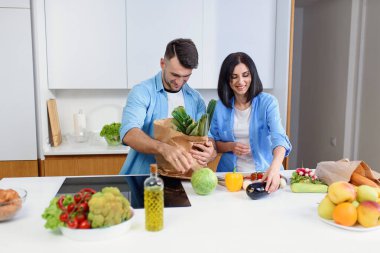 Genç çift, sıcak mutfakta marketten taze ürünleri birlikte indiriyor..