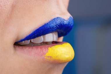 Mavi ve sarıya boyanmış güzel ve tombul kadın dudaklarına yakın çekim. Ukrayna bayrağı renginde tanımlanamayan bir kadının dudakları.