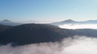 Mavi gökyüzü altındaki bulutların arasındaki dağların havadan görünüşü Çek Cumhuriyeti 'ndeki ulusal peyzaj parkında gün doğumu. Bulutların üstünde.