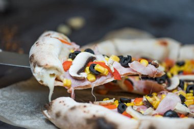 Biberli, zeytinli, jambonlu, mantarlı, kırmızı biberli ve mısırlı lezzetli pizza dilimleri. Kalın kenarlı bir pizzanın yakın çekimi. Amerikanvari.