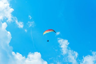 Gökyüzündeki paraglider açık mavi yaz gökyüzünde uçar. Güneşli bir günde dağlarda paraşütle atlamak.