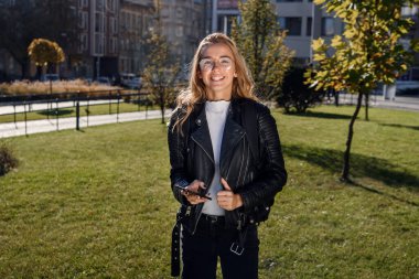 Güneşli bir günde sokakta yürürken akıllı bir telefonla mesaj yazan güzel bir kız..