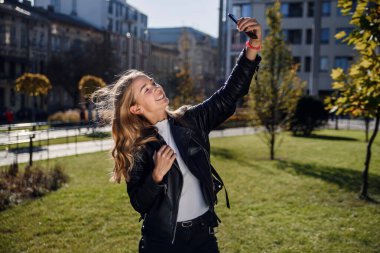 Neşeli, güzel öğrenci kız sokakta akıllı telefondan selfie çekiyor, dışarıda yürümekten hoşlanıyor..