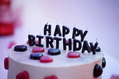 Siyah mumlarla süslenmiş doğum günü pastası Mutlu yıllar yazıtları ve jöle şeklinde siyah ve kırmızı kalpler..