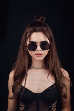 Yarı şeffaf siyah elbise ve siyah arka planda güneş gözlüğü takan güzel, çekici bir kız..