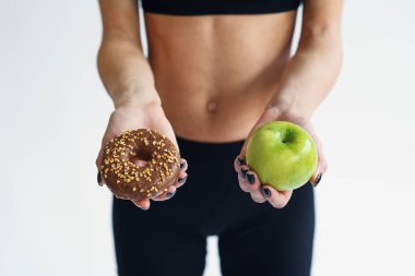 Mükemmel bir vücudu olan, donut ve elma tutan sportif bir kadın. Sağlıklı düşük kalorili yemekler, taze meyveler. Diyet, sağlıklı bir yaşam tarzı..